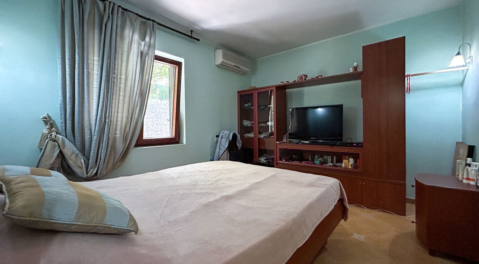 Bedroom with a double bed and furniture in a villa in Dobrota, Montenegro: interior view with a TV wall unit and window.