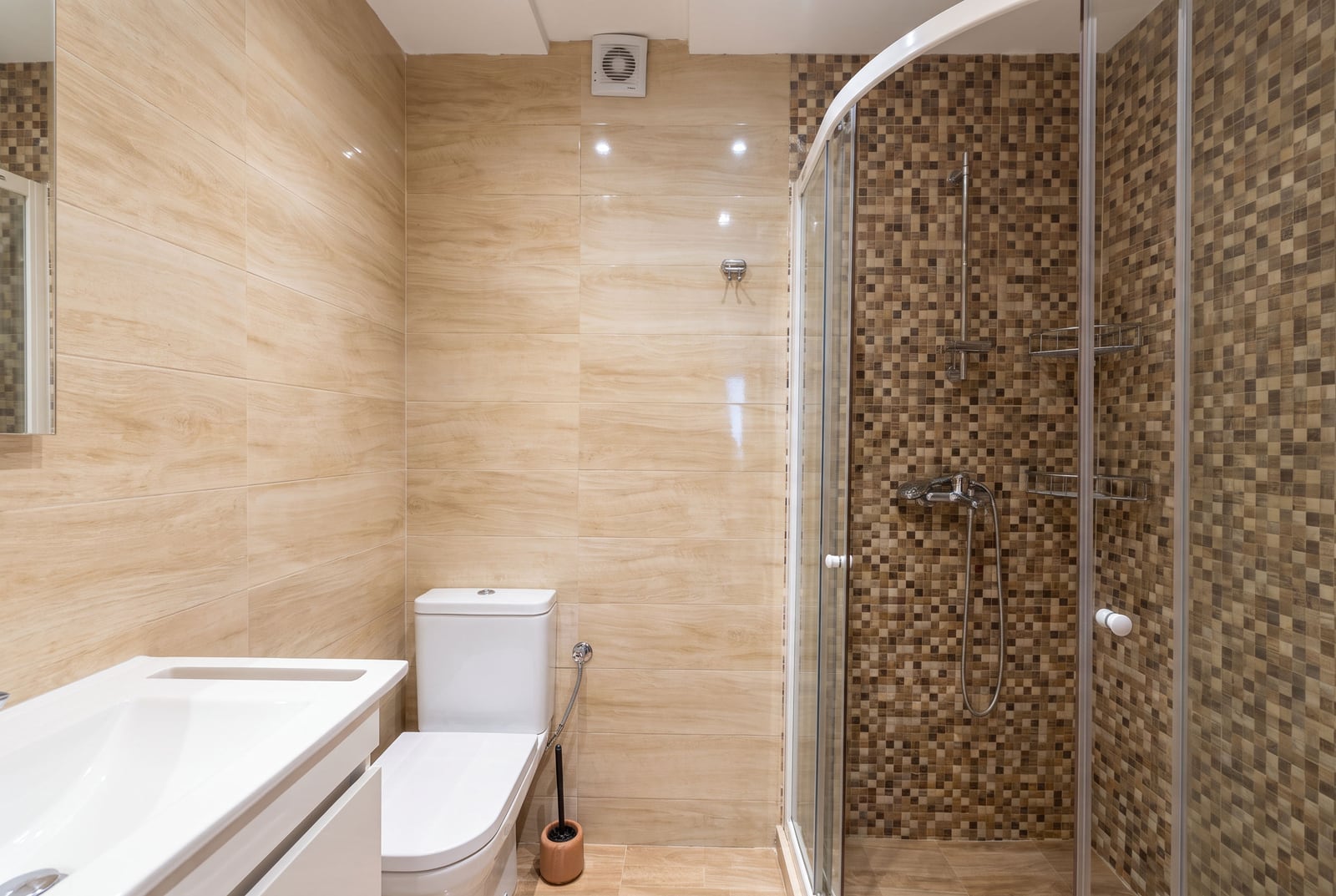 Bathroom featuring a white toilet, sink vanity, and glass shower enclosure with mosaic tiles.