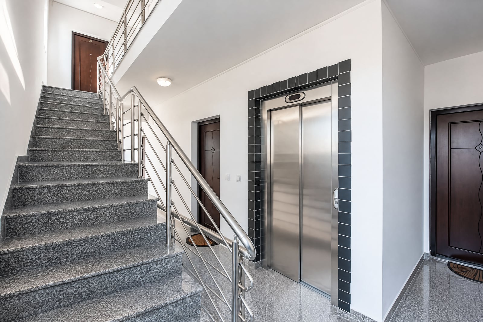 Granite staircase with metal railing next to a stainless steel elevator in a building hallway.