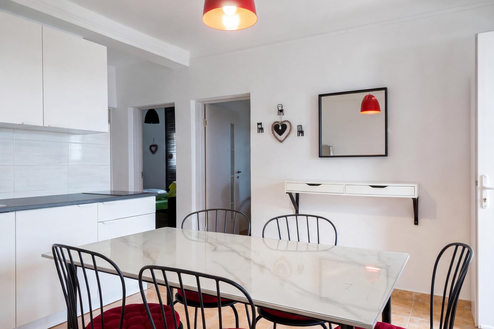 Kitchen area with white cabinets, a marble dining table, black chairs with red cushions, and a red pendant light.