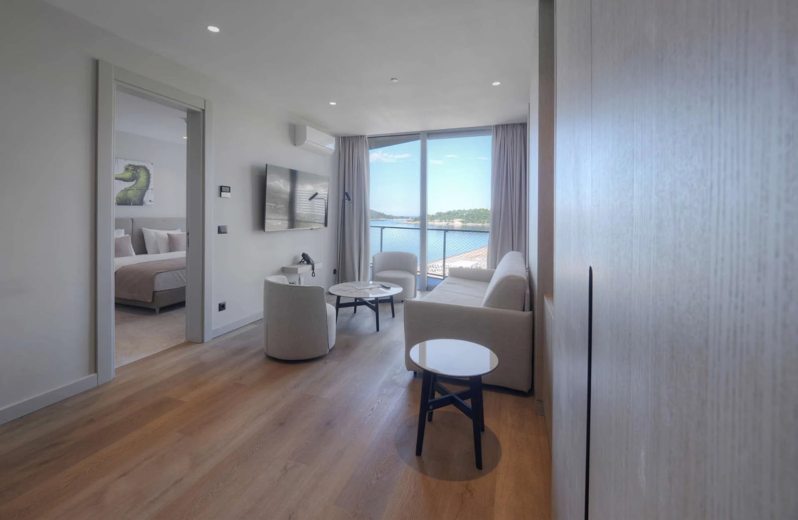 Bright living room with sofa, armchairs, and TV, featuring a sea view through large glass windows.