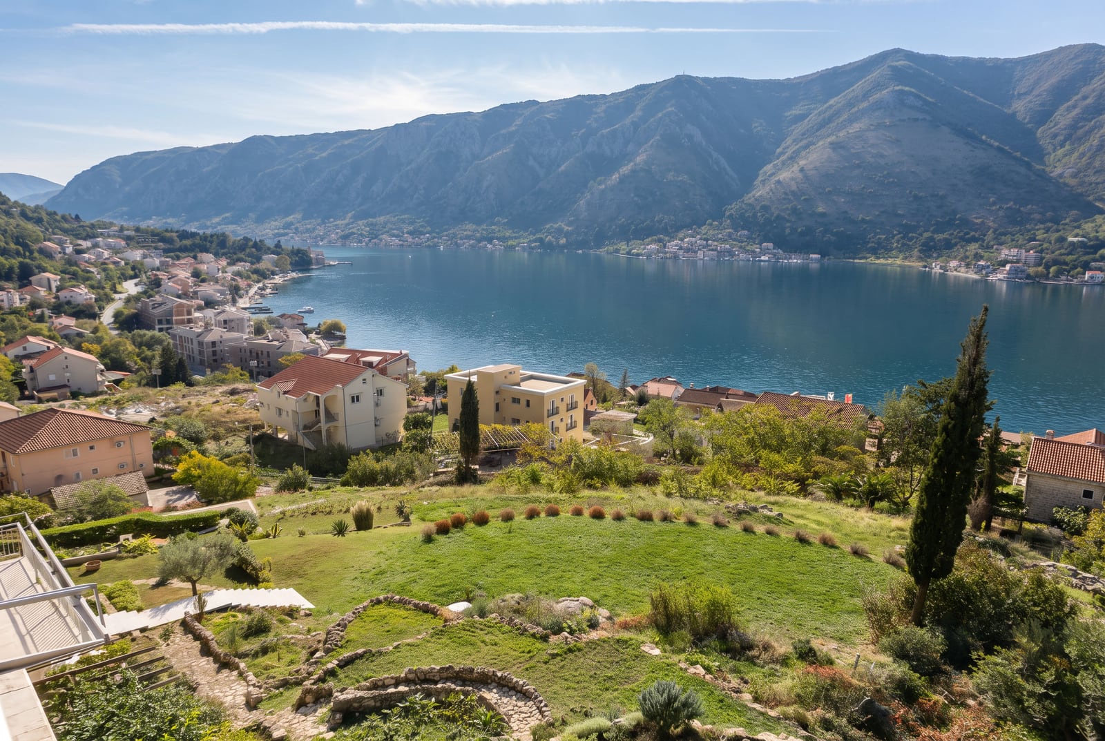 Panoramic view of a bay, mountains, and coastal houses with a terraced garden in the foreground.