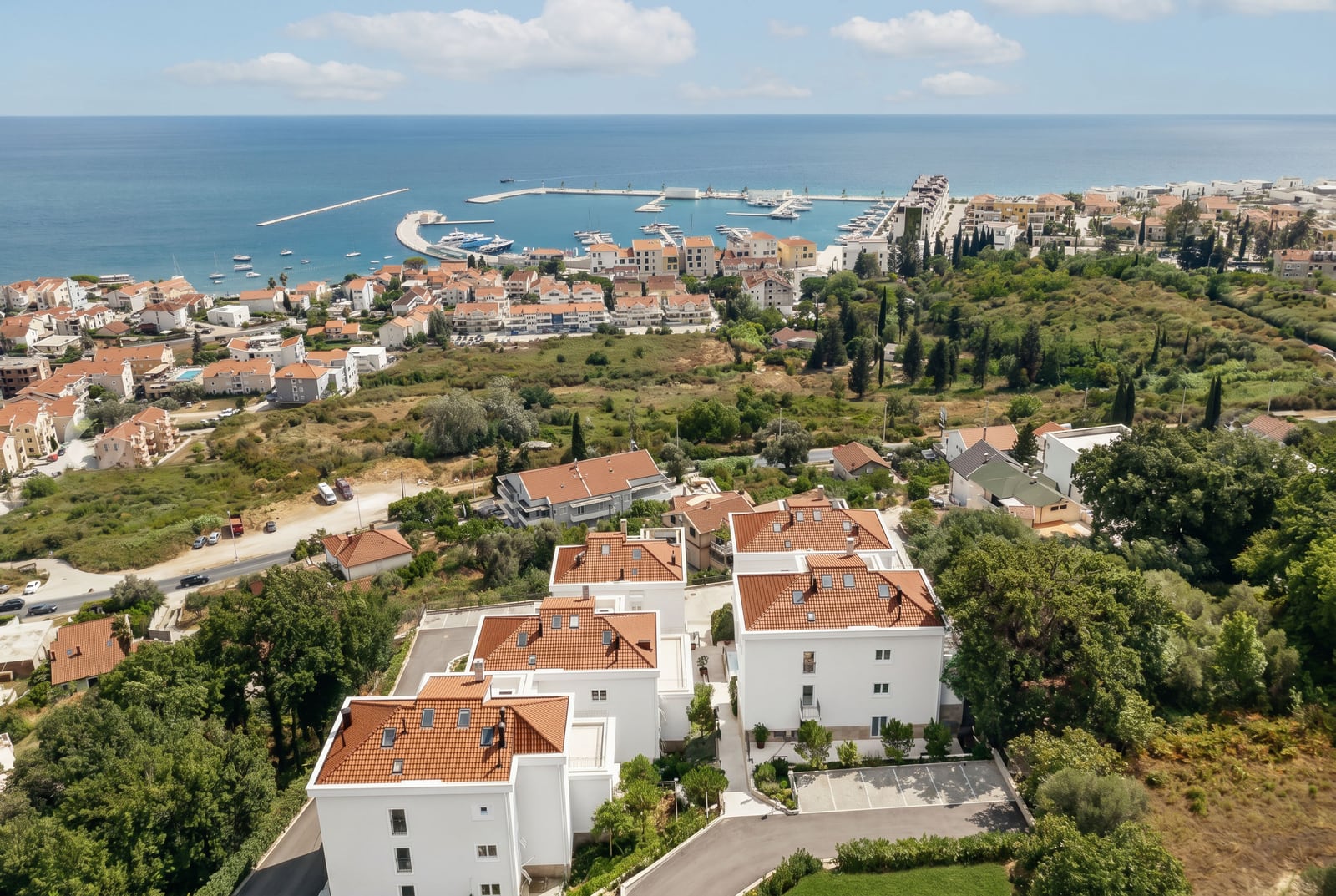 Aerial view of a residential complex in Kumbor, Montenegro: white houses with tiled roofs and a panoramic view of the sea and marina