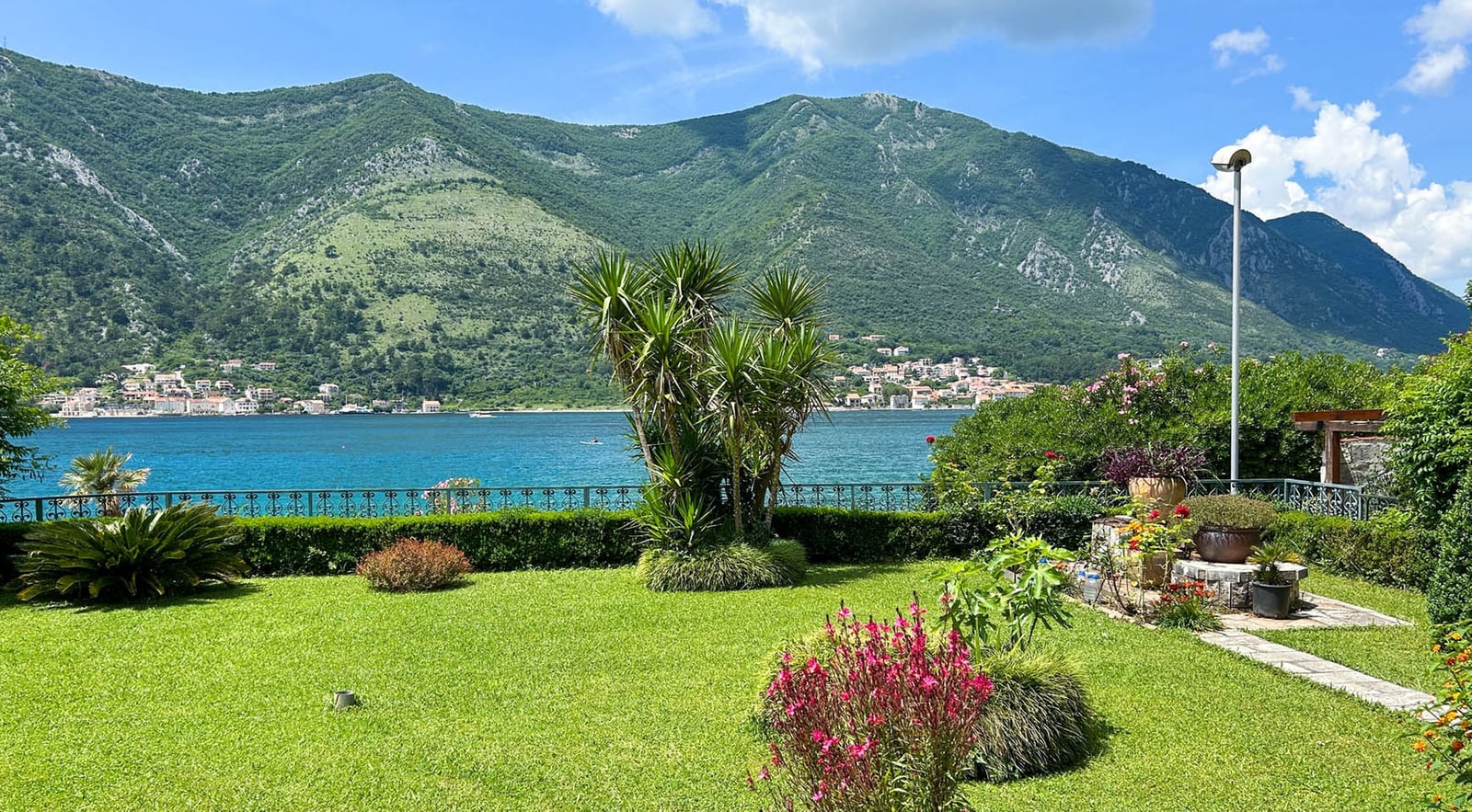 Green garden of a villa in Dobrota, Montenegro, with panoramic views of Kotor Bay and the mountain landscape.