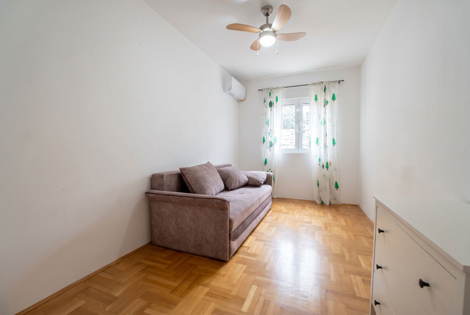 Bright bedroom with a sofa and parquet flooring in an apartment for sale in Budva, Montenegro. Ceiling fan installed.