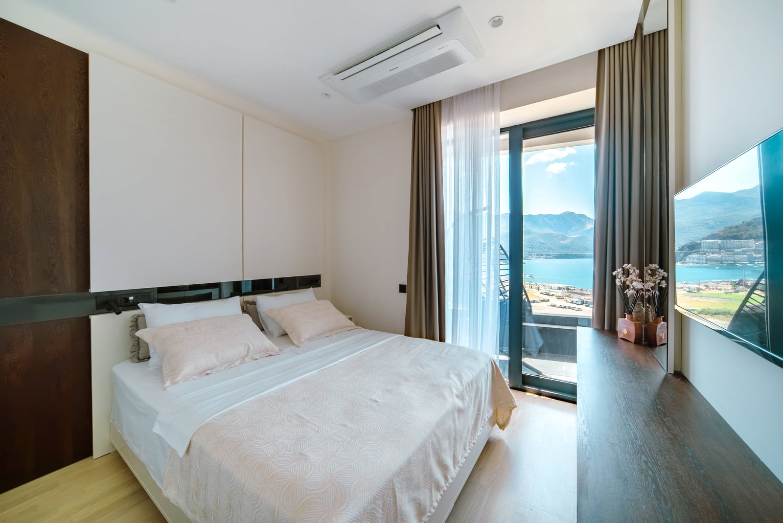 Modern bedroom with sea and mountain views in the Bečići residential complex, Montenegro: double bed, TV, and panoramic window.