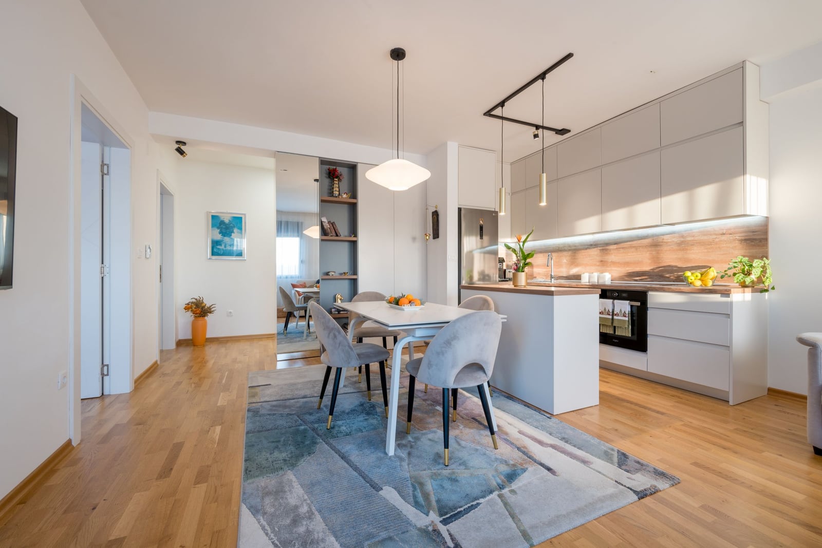 Modern open-plan kitchen and living room in an apartment, Tivat, Montenegro: light-colored furniture, dining area, and parquet flooring.
