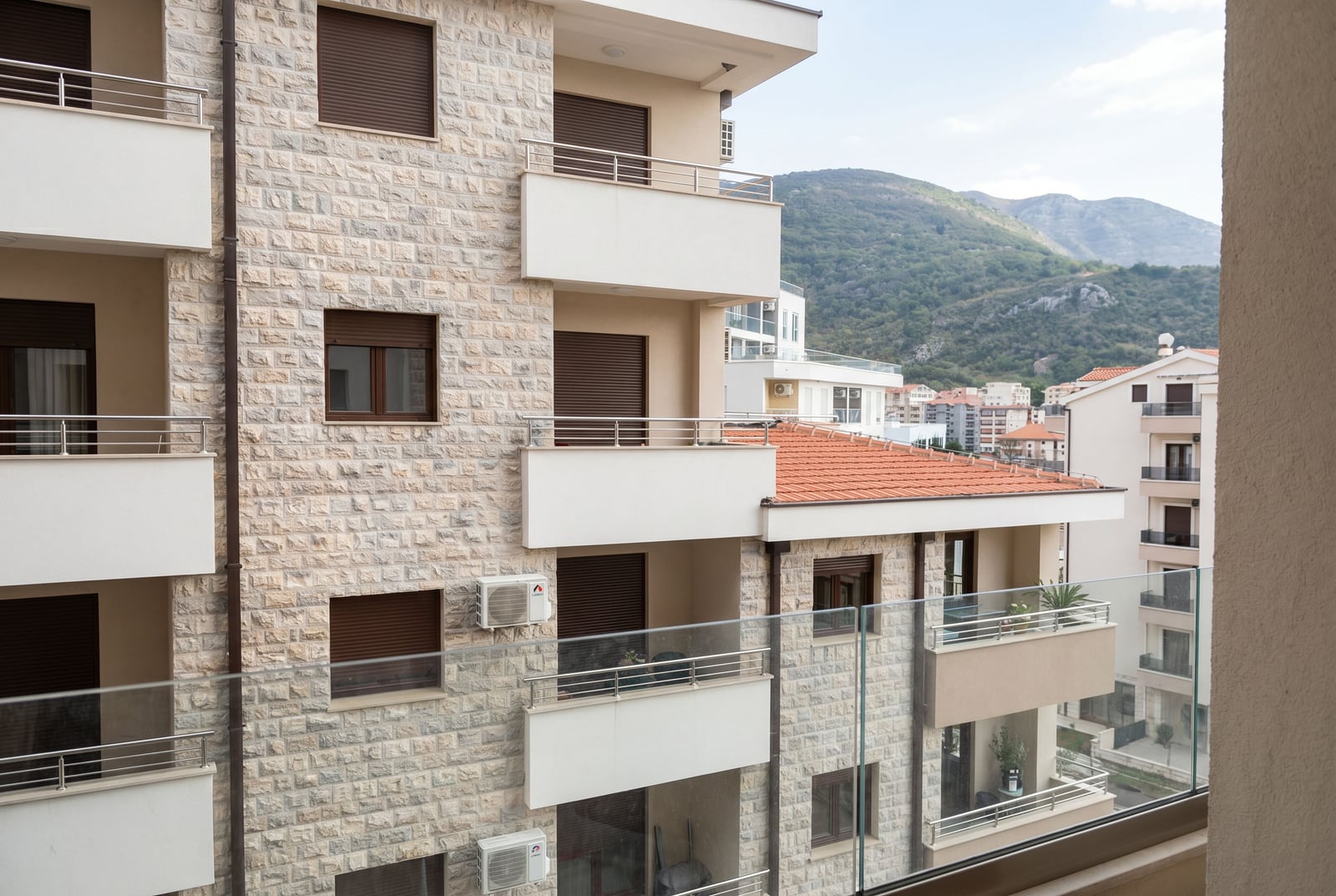 Stone residential building facade with balconies in Bečići, Montenegro, with a view of neighboring buildings and mountains.