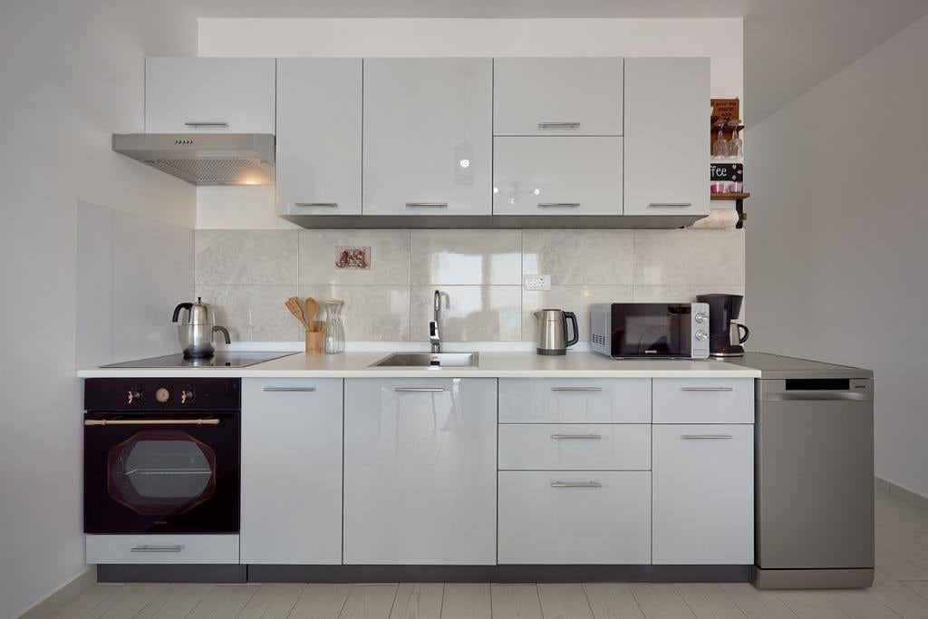 Modern bright kitchen in an apartment in Pržno, Montenegro: glossy cabinets, built-in appliances, and a dishwasher.
