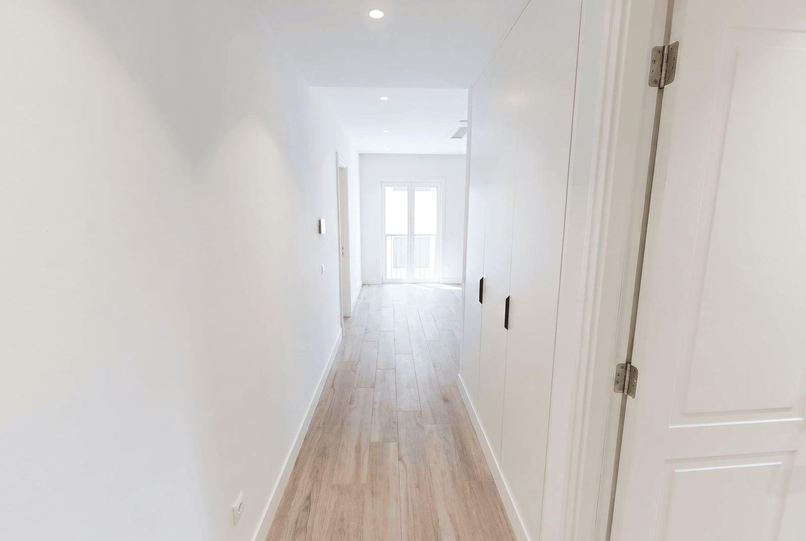 Bright hallway with white built-in wardrobes and wooden flooring in a new apartment, Luštica, Montenegro.