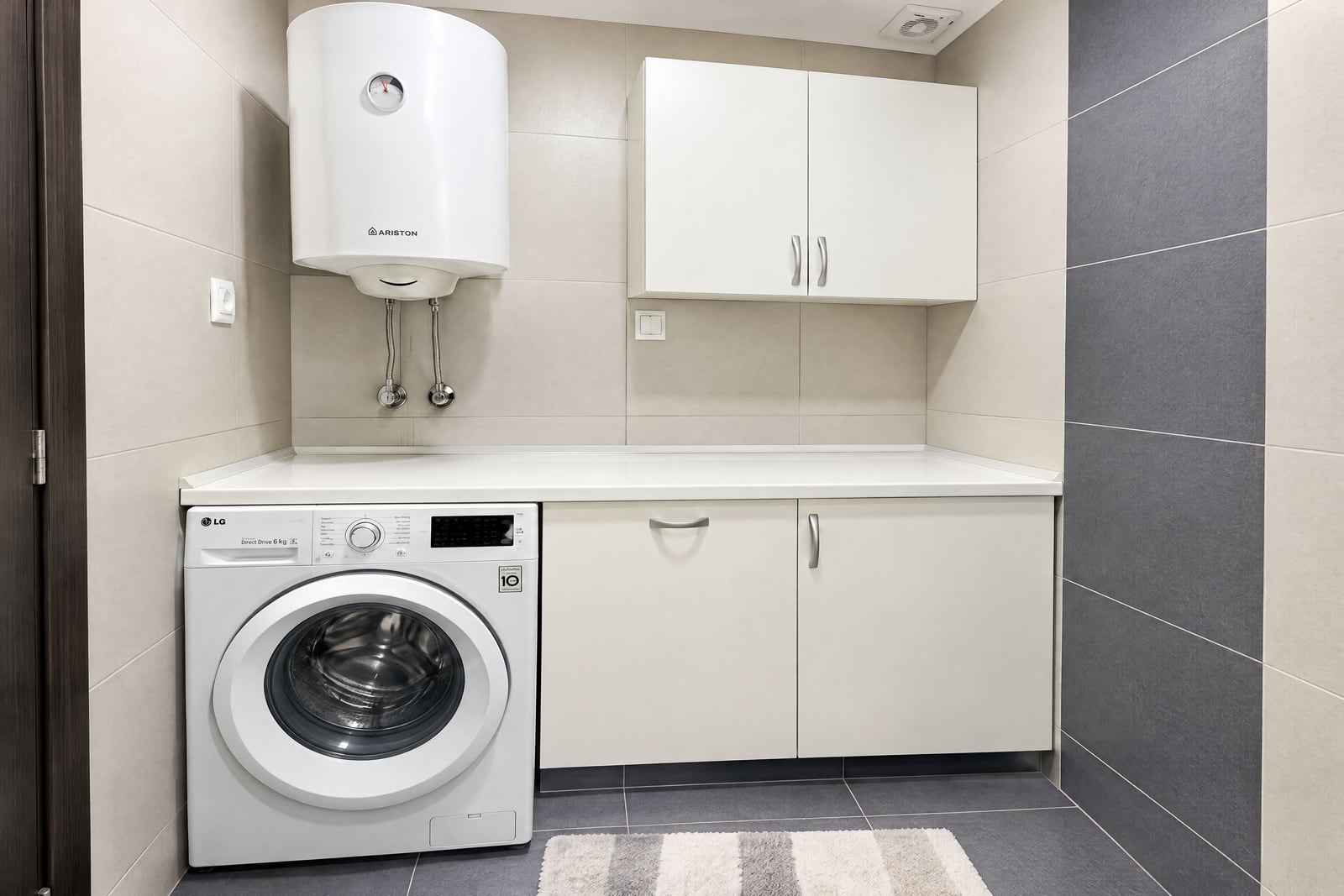 LG washing machine, wall-mounted Ariston boiler, and white cabinets against tiled walls.