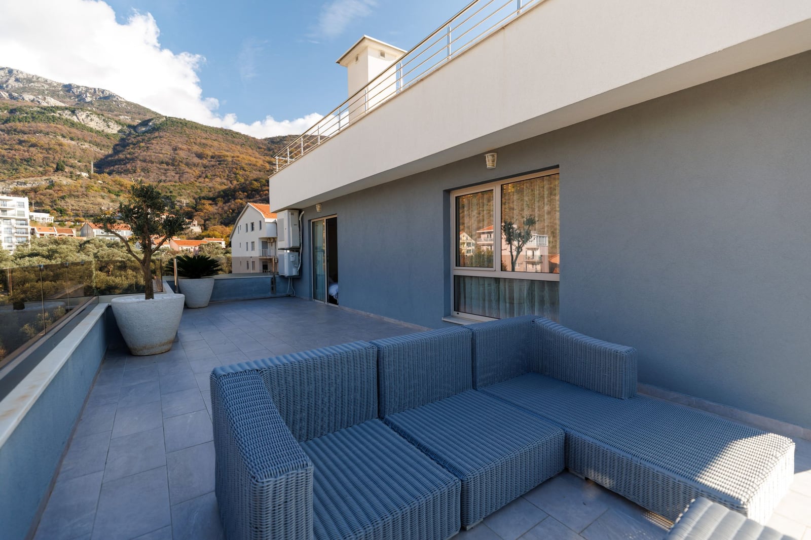 Spacious penthouse terrace in Bečići, Montenegro, featuring wicker furniture, mountain views, and modern design.