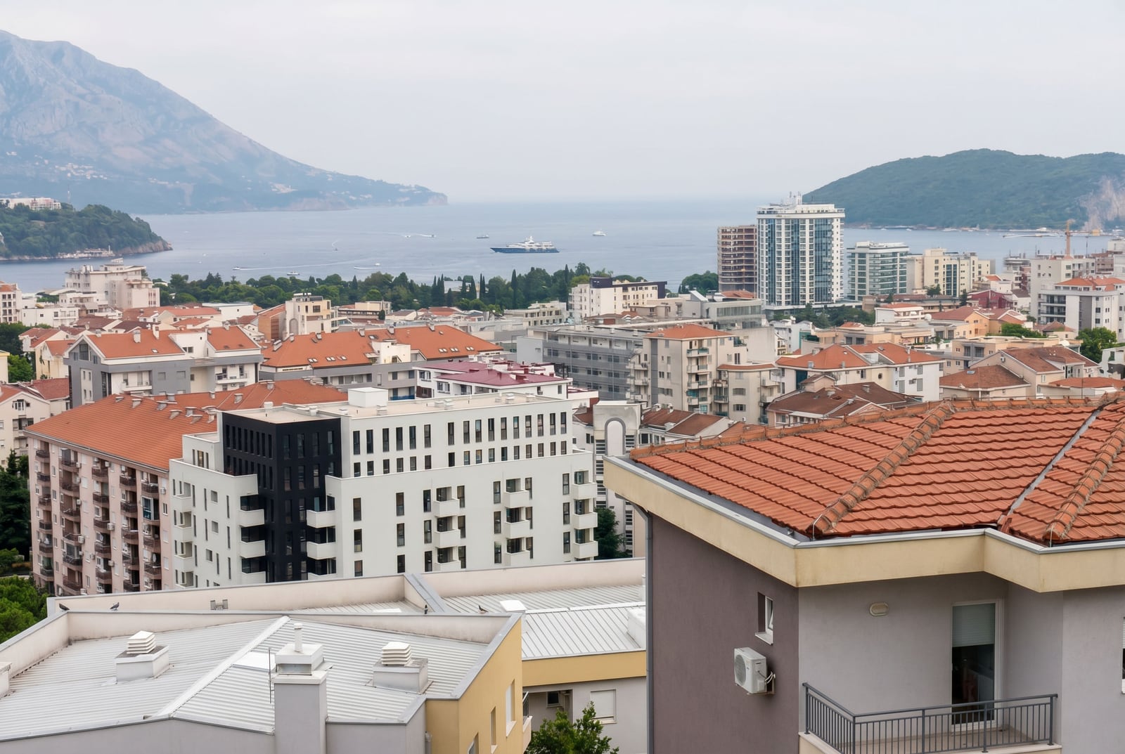 Panoramic view of the city, tiled rooftops, sea, and mountains in Budva, Montenegro.
