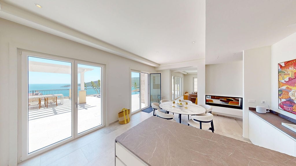 Bright living room with a terrace and sea view in a villa, Luštica, Montenegro: marble table, modern kitchen, and fireplace.