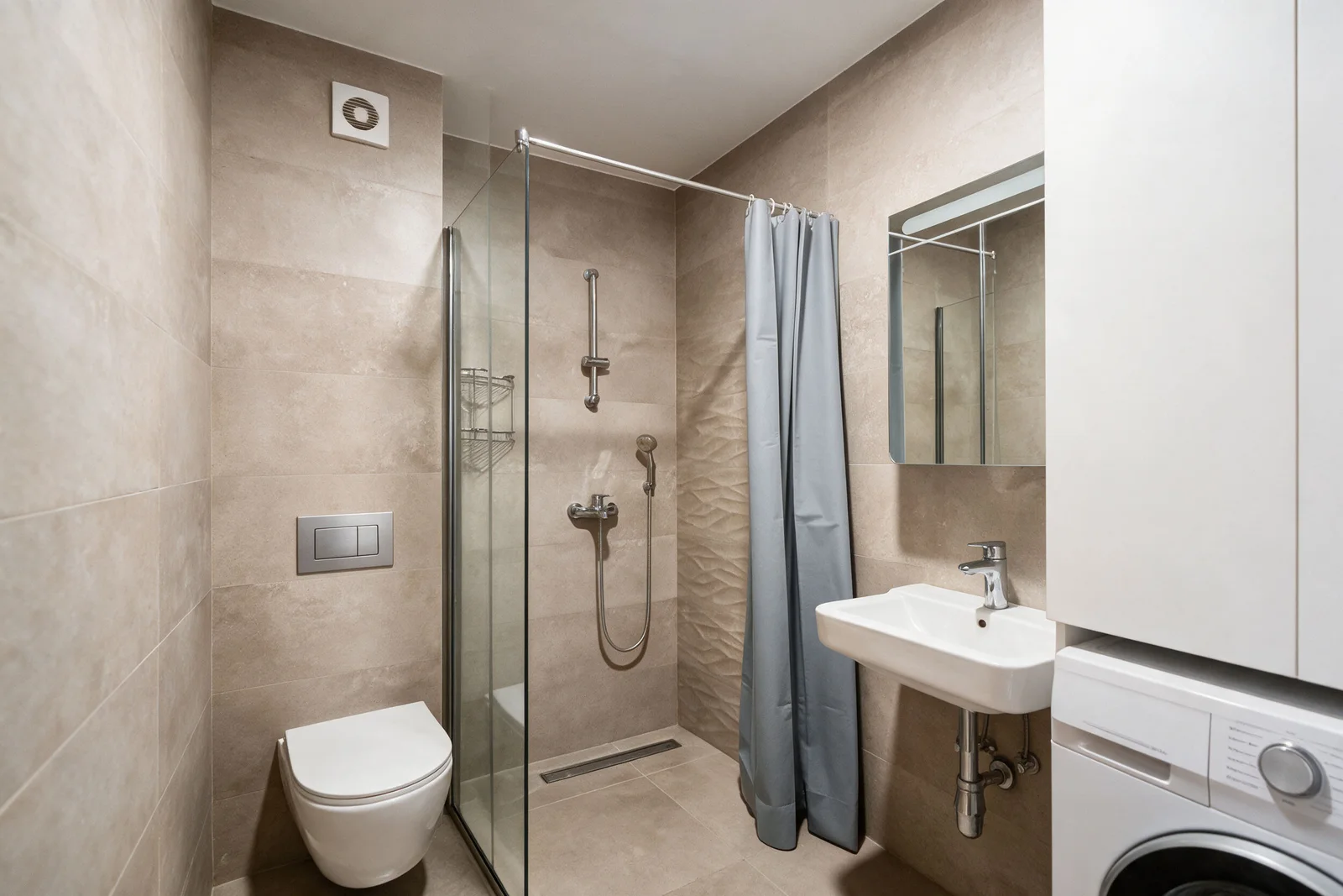 Bathroom featuring a shower, wall-mounted toilet, sink, and washing machine on beige tiles.