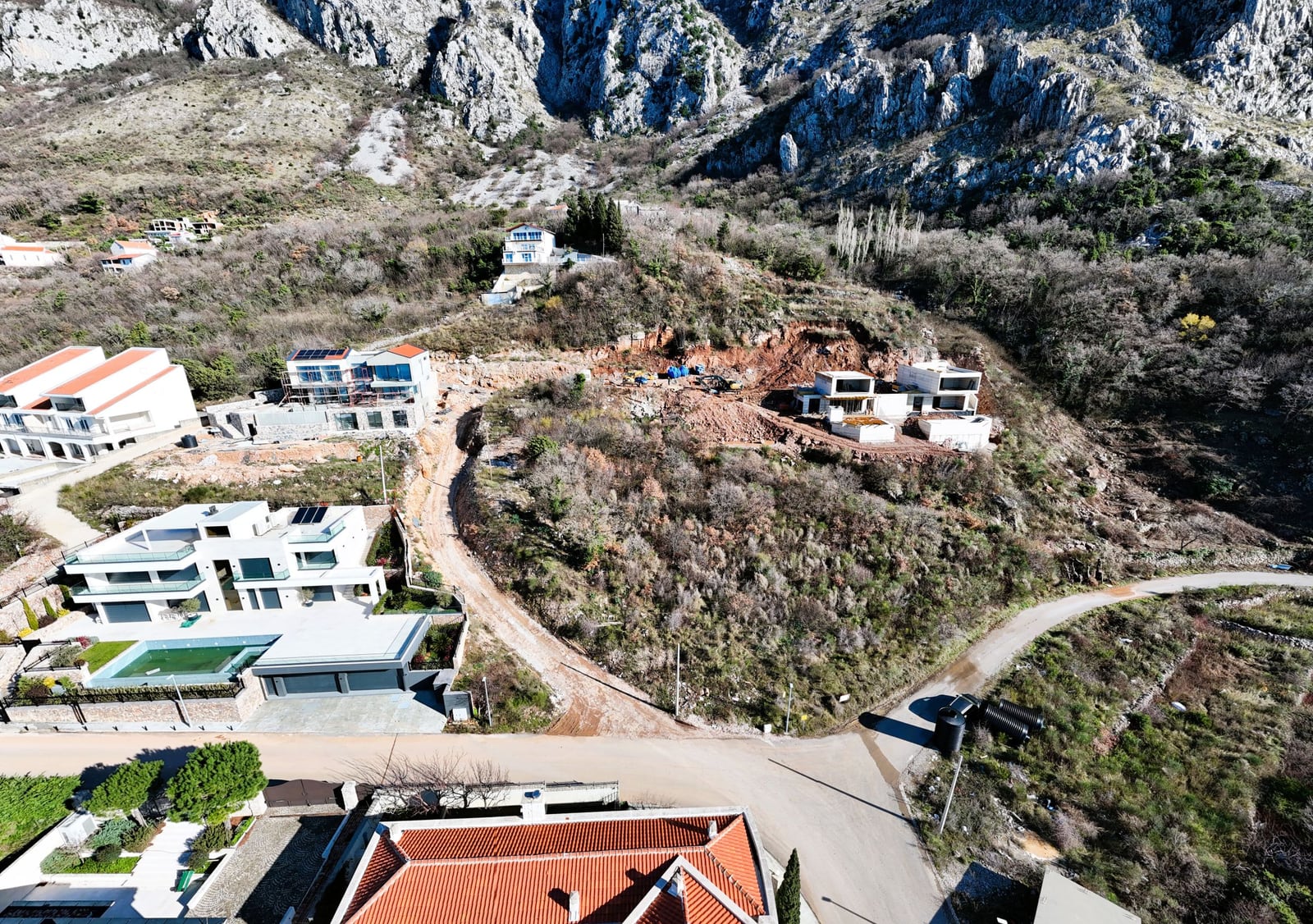Aerial view of a land plot in Blizikuće, Montenegro: modern villas with swimming pools and mountain landscape.