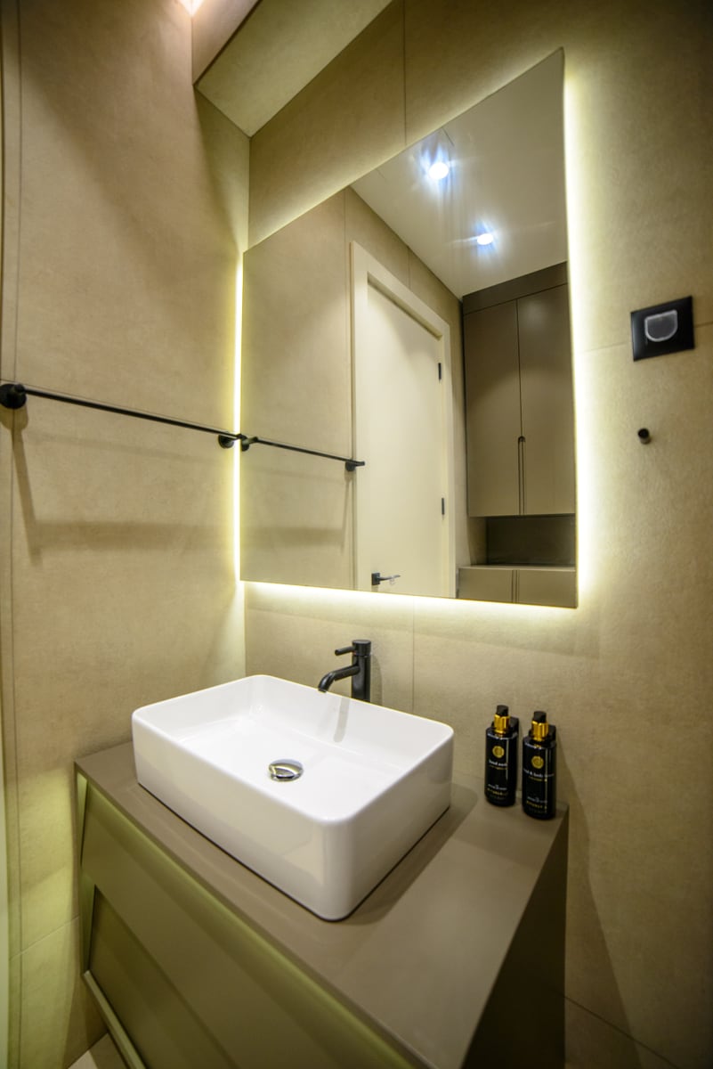 Modern bathroom in an apartment, Bečići, Montenegro: countertop sink, black faucets, and a mirror with lighting.