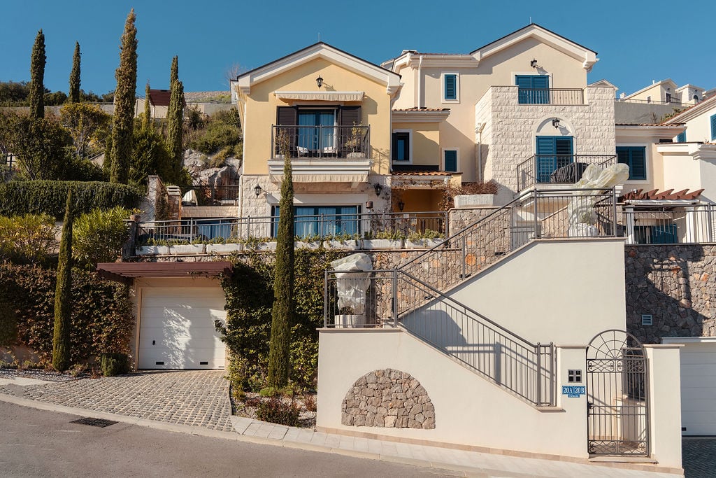 Two-story townhouse in Luštica Bay, Montenegro: stone facade, balconies, garage, and landscape design on a hillside.