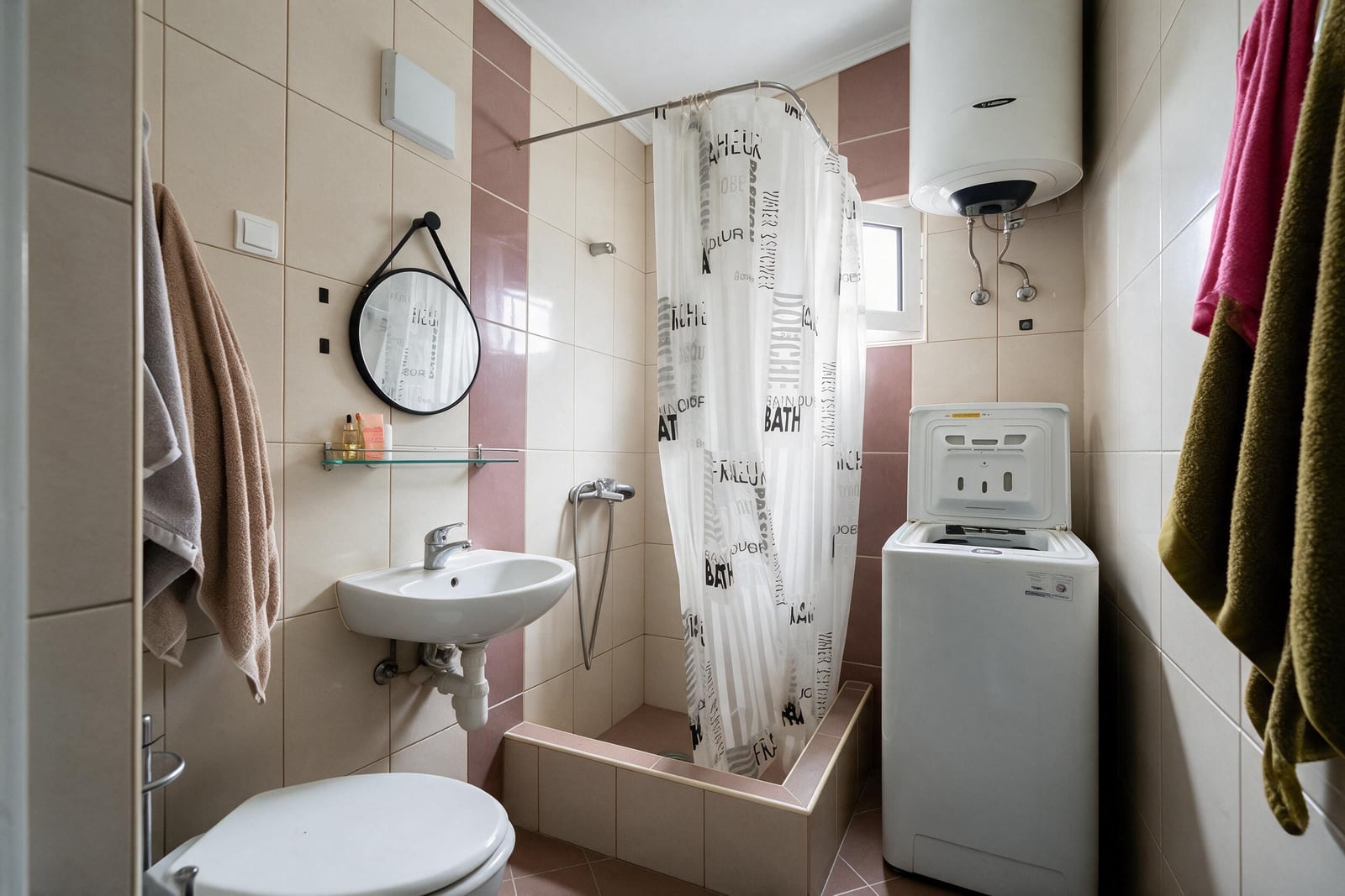 Bathroom featuring a toilet, sink, shower curtain, wall-mounted water heater, and washing machine against tiled walls.