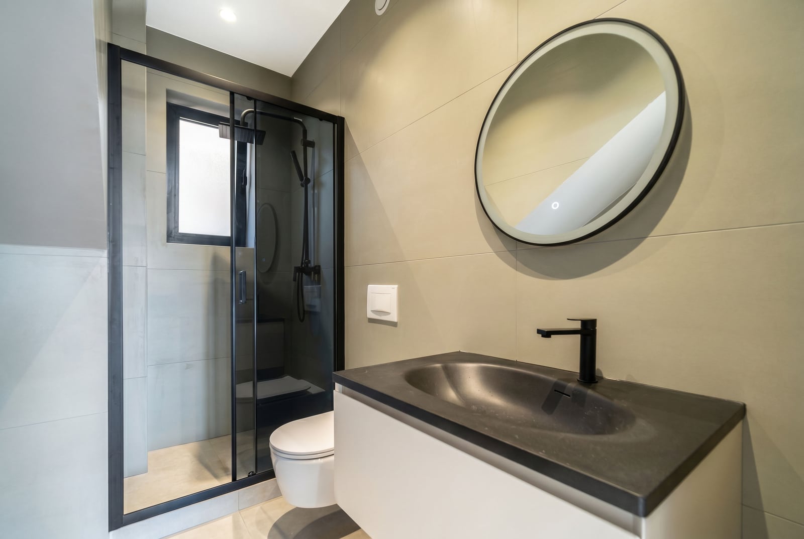 Modern bathroom in a townhouse, Kavač, Montenegro: walk-in shower, black fixtures, and a round mirror.