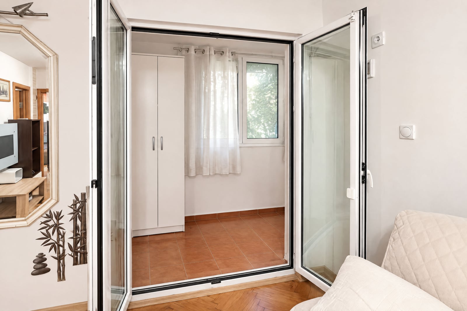 View from a living area into an enclosed loggia featuring a white wardrobe and terracotta tiles.