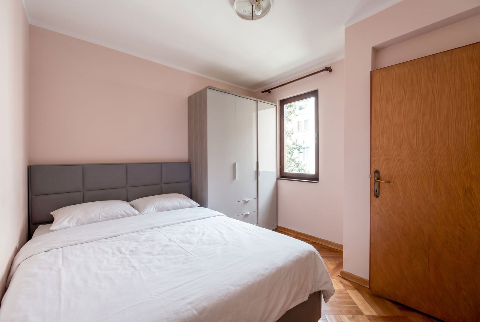 Cozy bedroom with a double bed and wardrobe in an apartment for sale in Budva, Montenegro. Parquet flooring and light-colored walls.