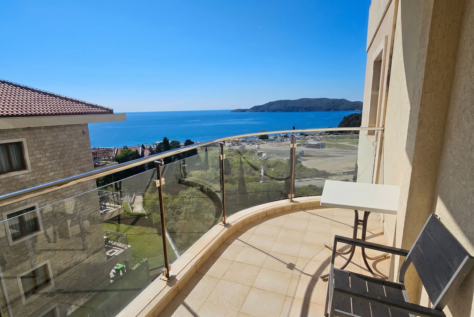 Balcony with panoramic sea view in the Bečići residential complex, Montenegro: table, chairs, and glass railing.