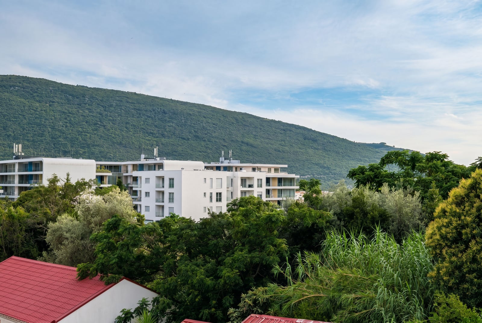 View of modern residential complexes and green mountains in Kumbor, Montenegro, panorama of the area with lush vegetation.