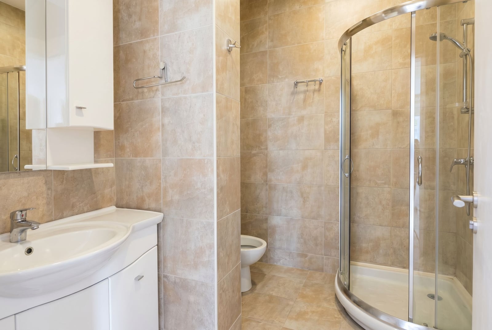 Bathroom in an apartment, Rafailovichi, Montenegro: white furniture, a shower cabin, and beige tiles in the interior.