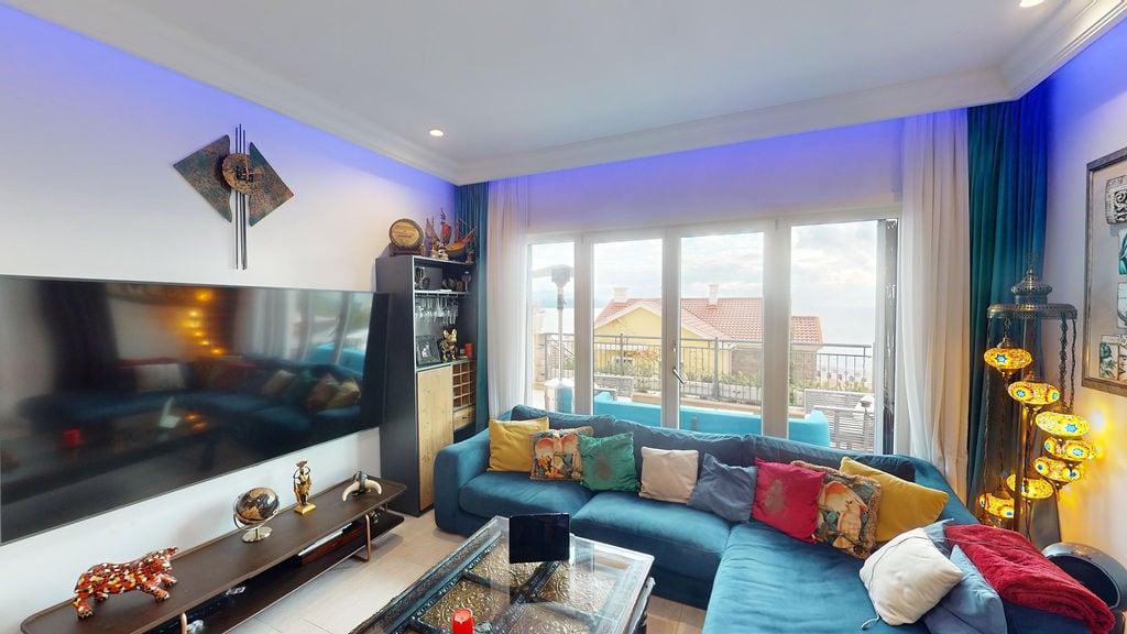 Living room in a townhouse in Luštica, Montenegro: blue sofa, TV, neon lighting, and a sea view through panoramic windows.