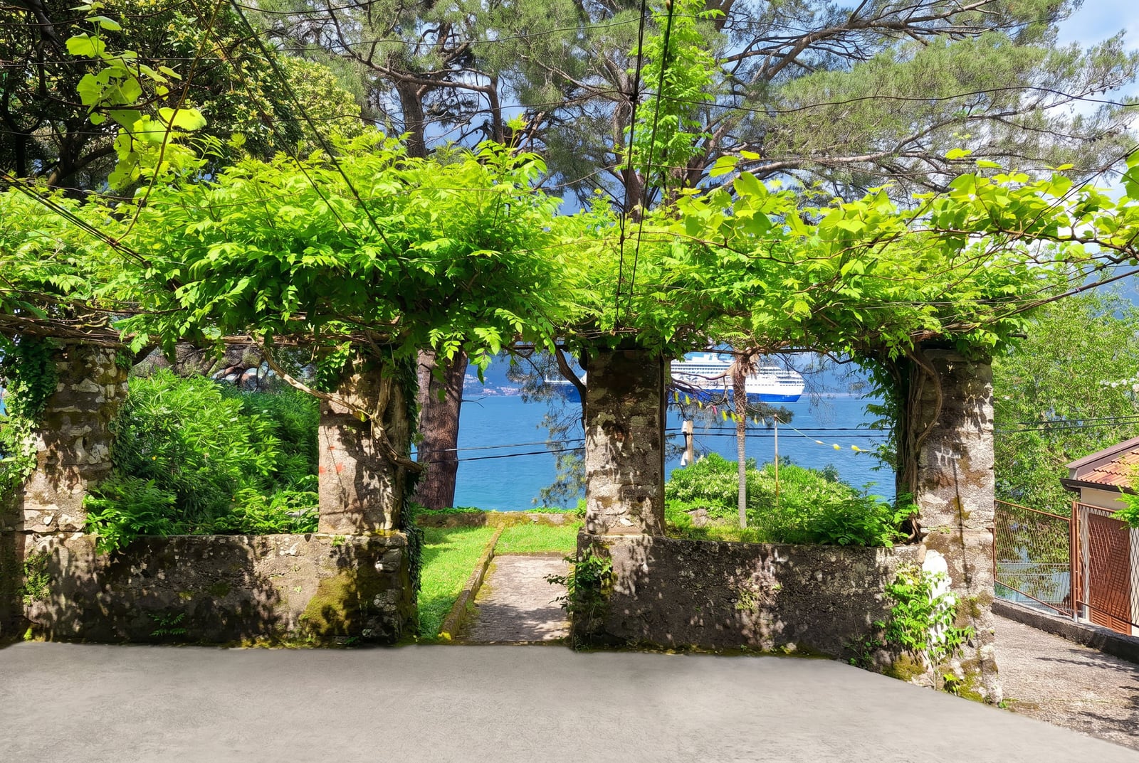 View of the sea and a cruise ship through a stone archway with grapevines on a property in Dobrota, Montenegro.