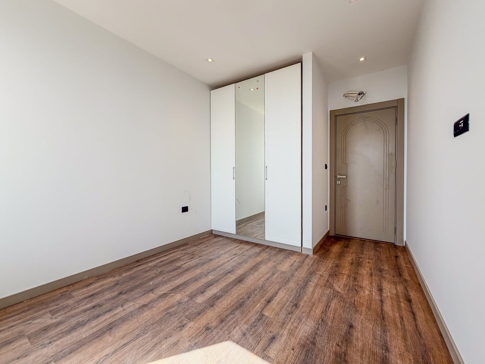 Empty room with wood flooring and a white built-in wardrobe with a mirror near the entrance door.
