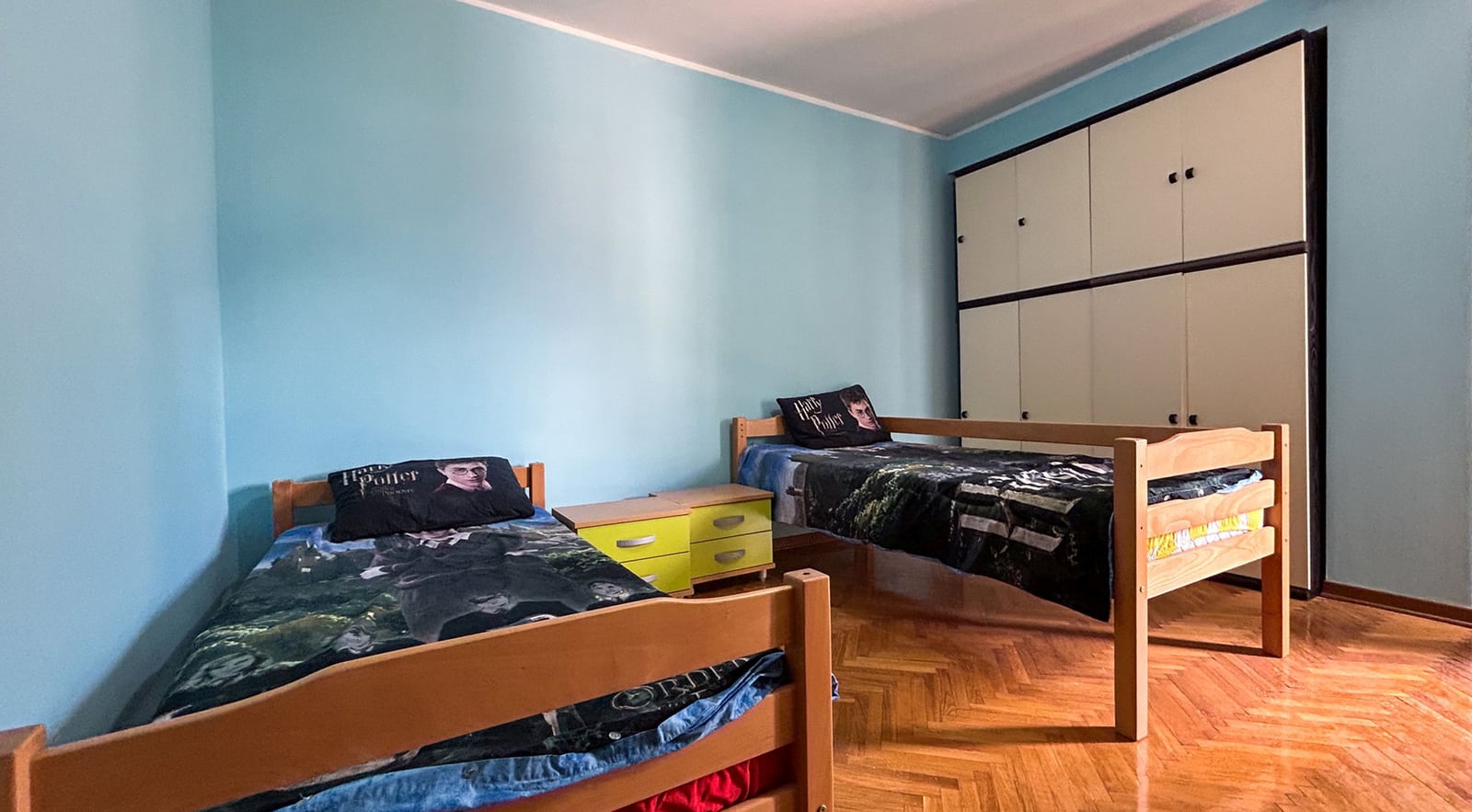 Children's bedroom with two beds and a built-in wardrobe in a villa in Dobrota, Montenegro. Parquet floor, blue walls.