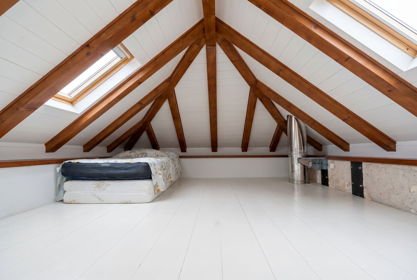Attic bedroom with wooden beams and a bed in an apartment in Budva, Montenegro. Bright interior with skylight windows.