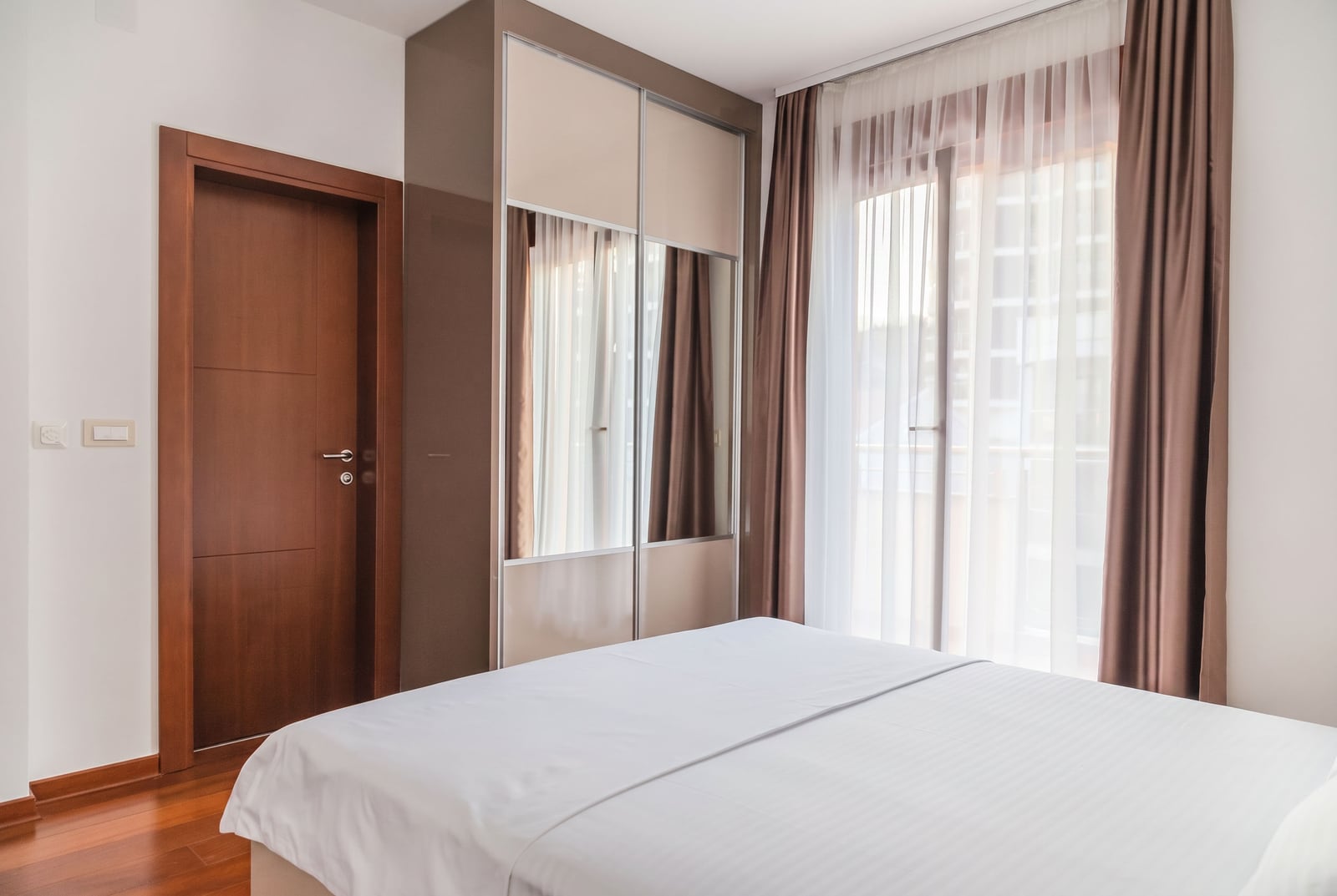 Modern bedroom with a double bed, mirrored wardrobe, and balcony access in an apartment, Becici, Montenegro.