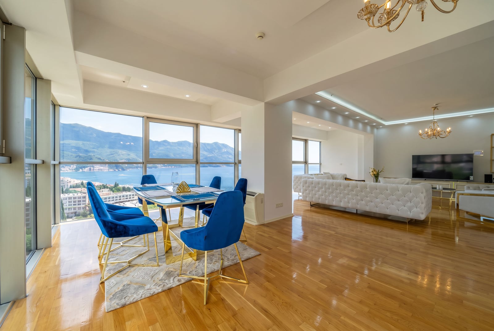 Spacious living room with panoramic windows, blue chairs, and a sea view in Budva, Montenegro