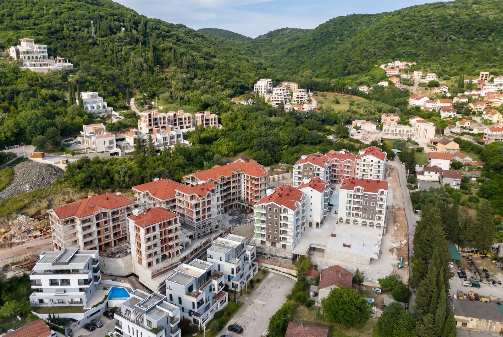 Aerial view of a residential complex under construction with red roofs, surrounded by mountains and greenery, Tivat, Montenegro.