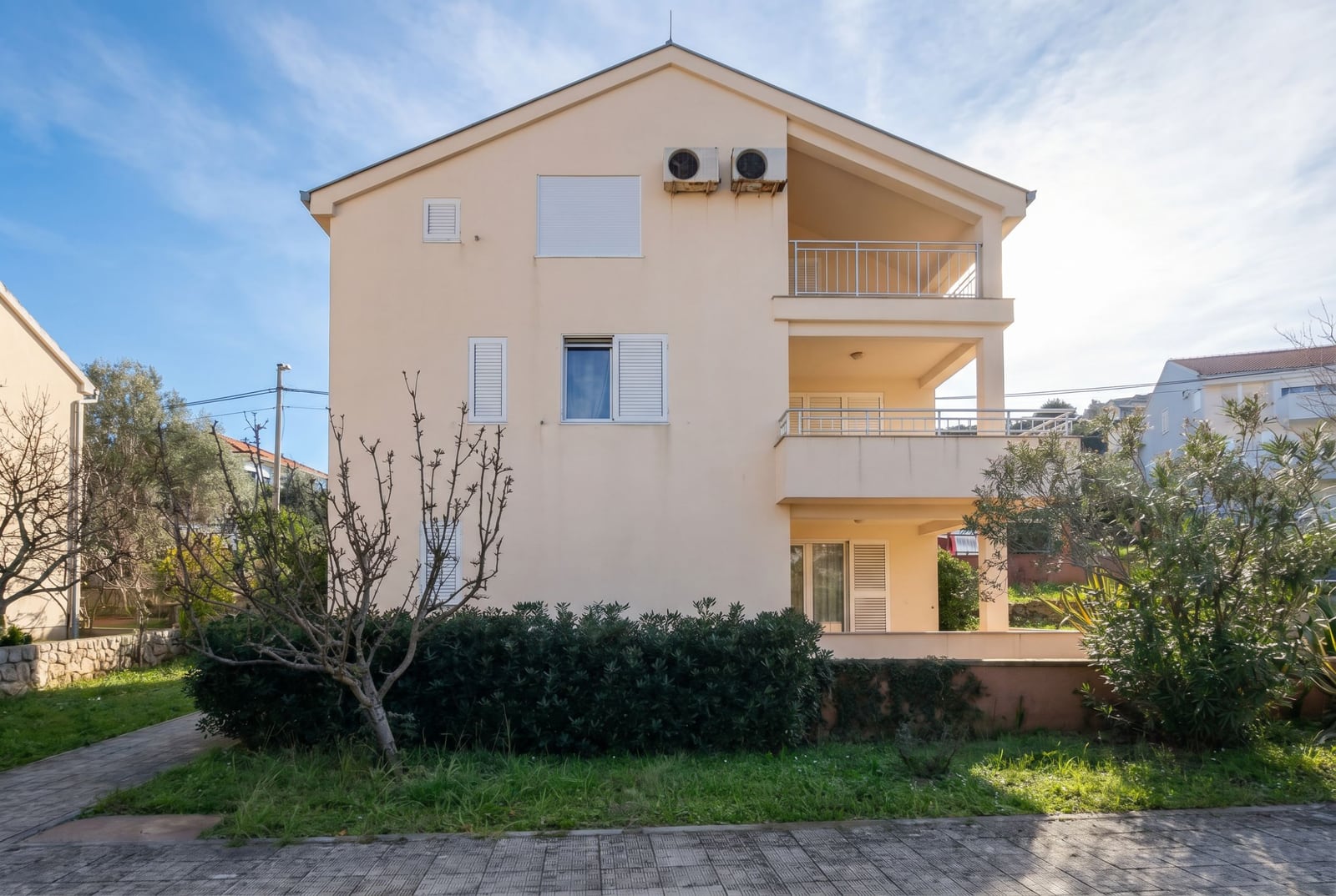 Three-story house with balconies and a garden in Baošići, Montenegro: building facade with air conditioners and white shutters.