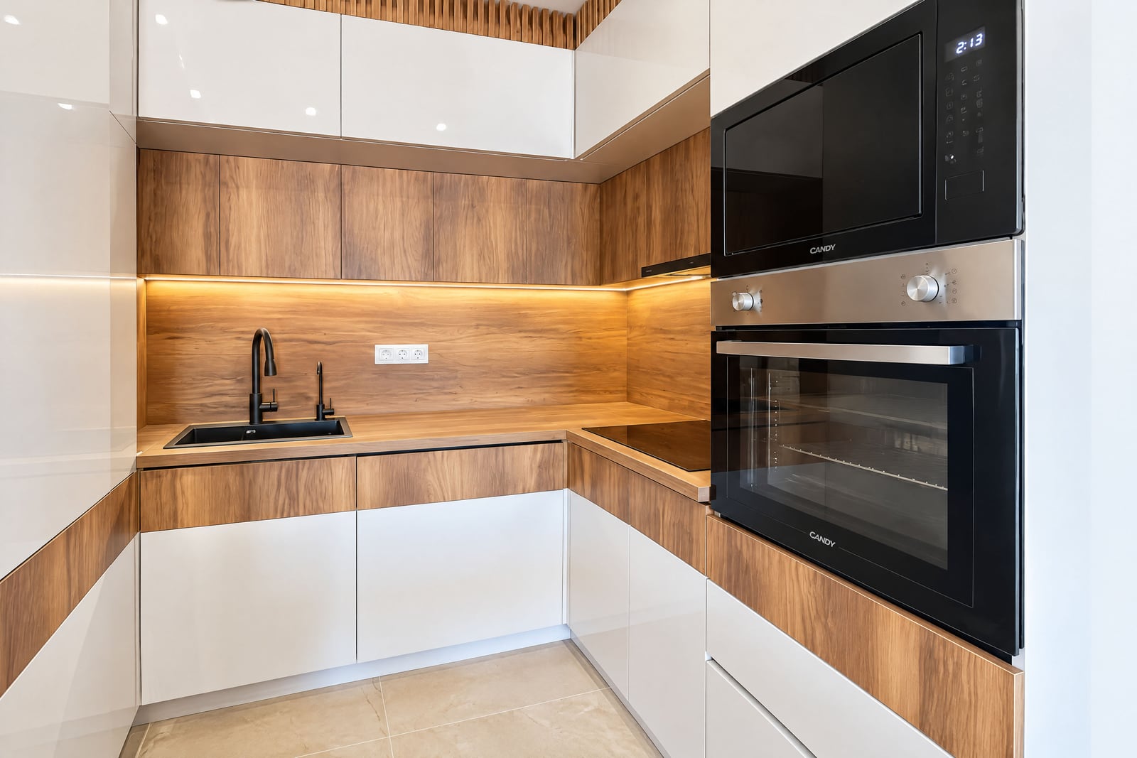 Modern kitchen featuring wood and white glossy cabinets, a black sink, induction cooktop, and built-in Candy oven and microwave.