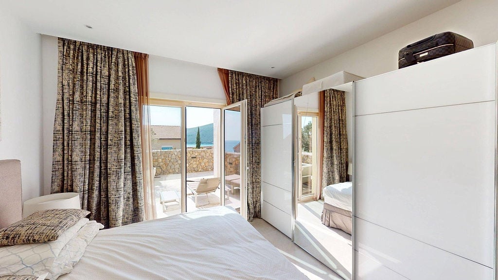Bedroom in an apartment in Luštica, Montenegro: white wardrobe, double bed, and access to a terrace with a sea view.