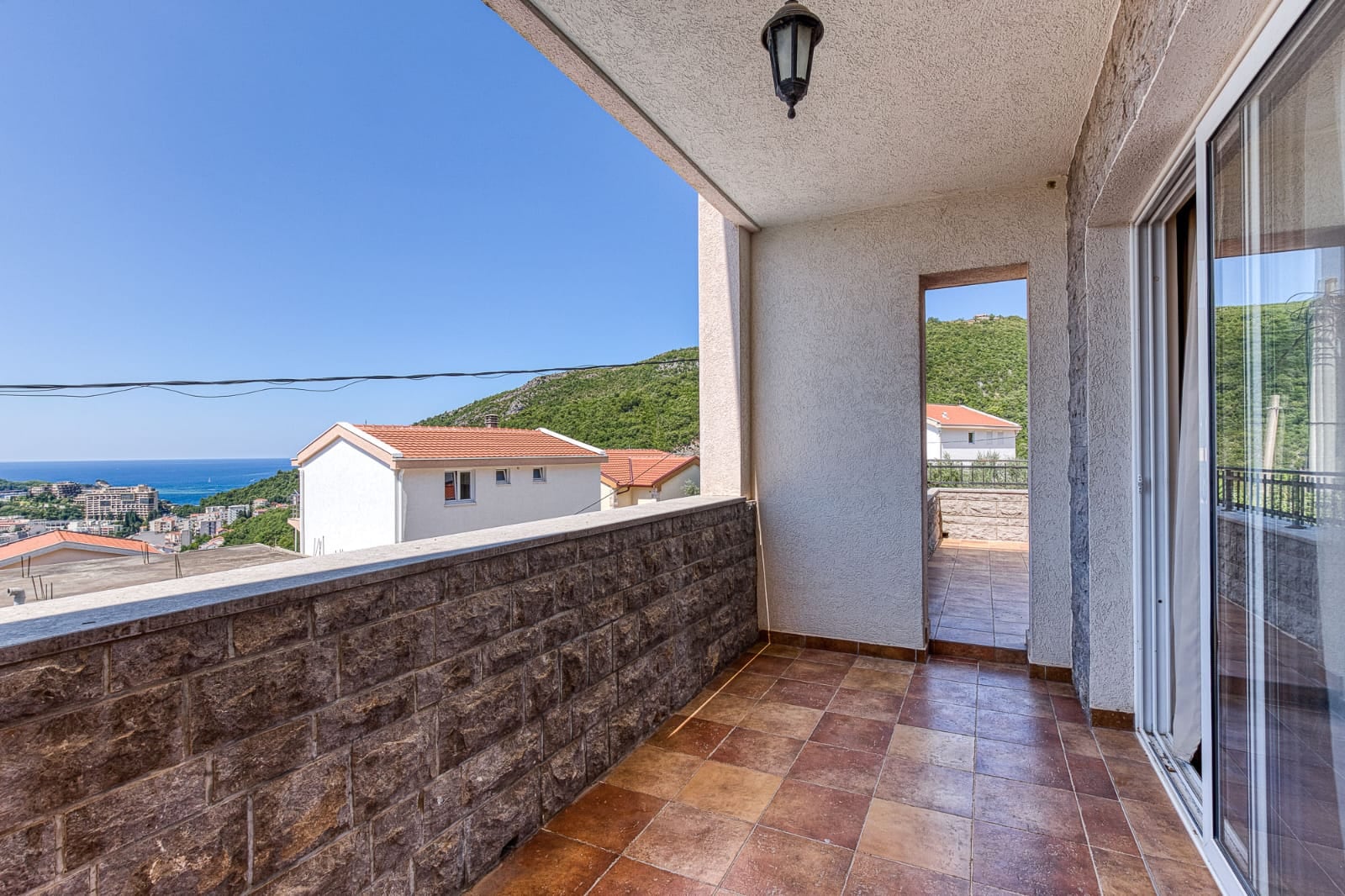 Spacious villa balcony in Becici, Montenegro, featuring stone finishes, tiled flooring, and panoramic views of the sea and mountains.