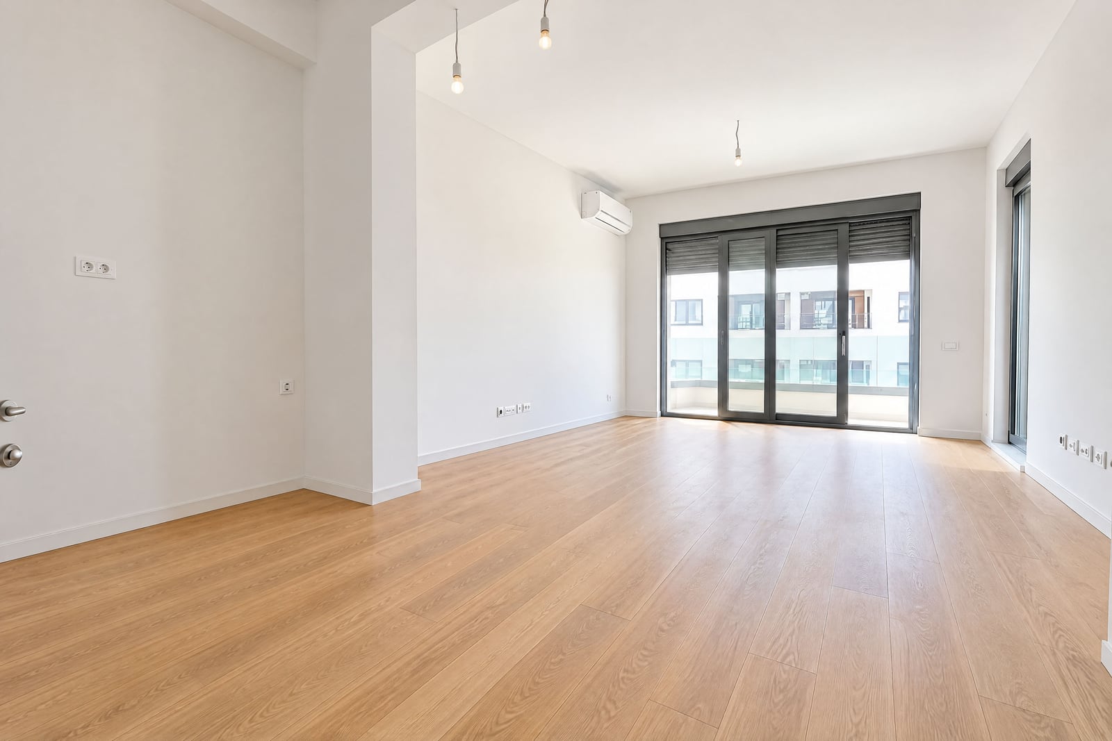 Empty room with wooden flooring, white walls, pendant lights, and large glass sliding doors.