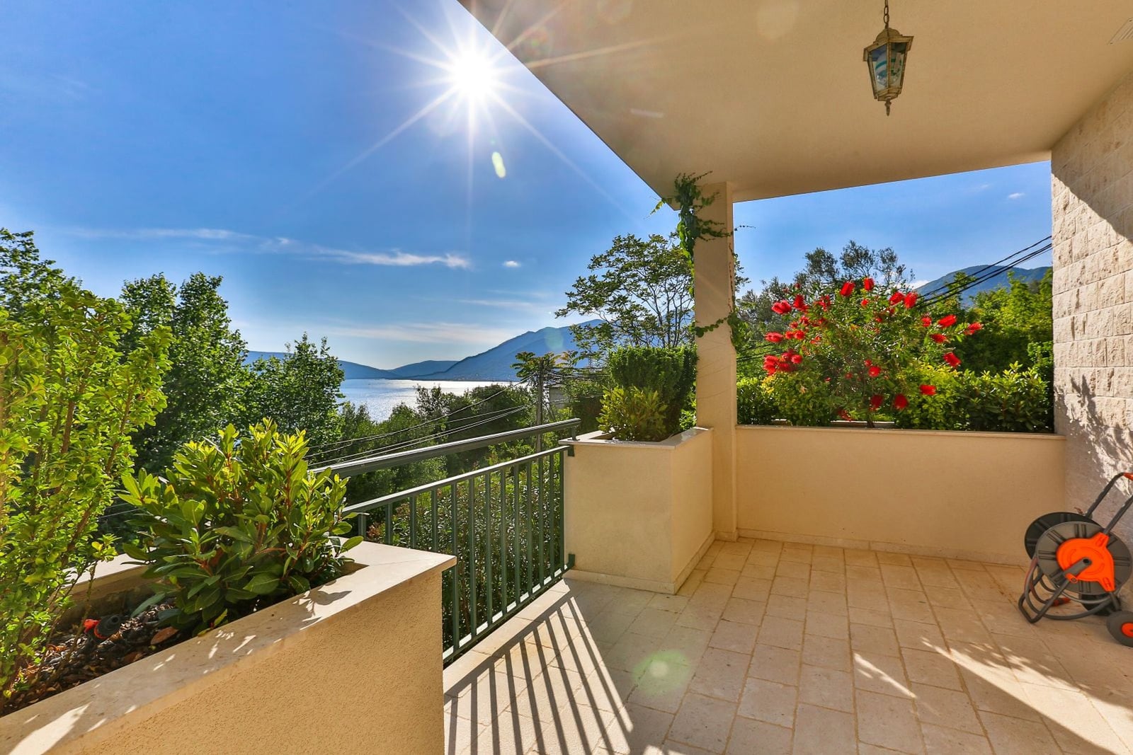 Spacious terrace of a villa in Tivat, Montenegro, with panoramic views of the sea, mountains, and a blooming garden.