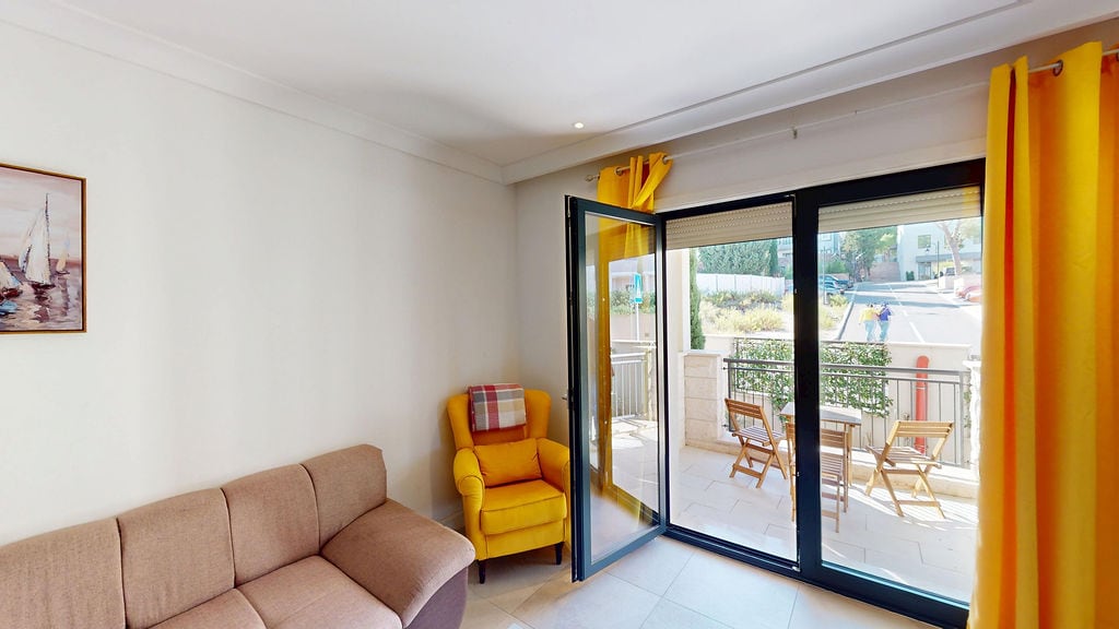 Living room in an apartment in Luštica, Montenegro: yellow armchair, beige sofa, and access to a furnished terrace.