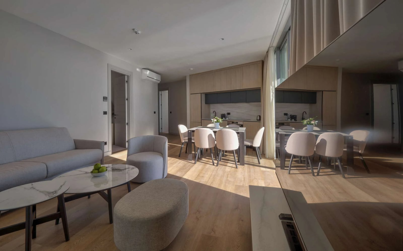 Modern living room with a grey sofa, marble table, and open kitchen visible in the background.
