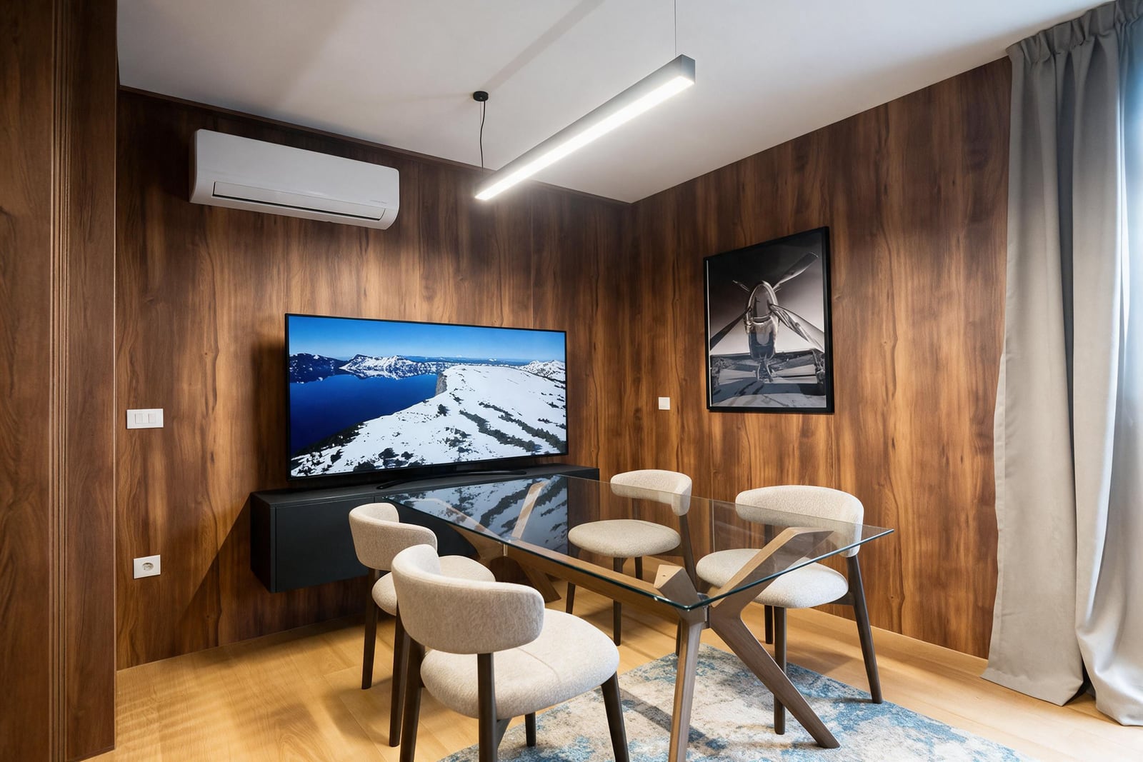Dining area with a glass table, four chairs, TV on wood-paneled wall, AC unit, and airplane artwork.