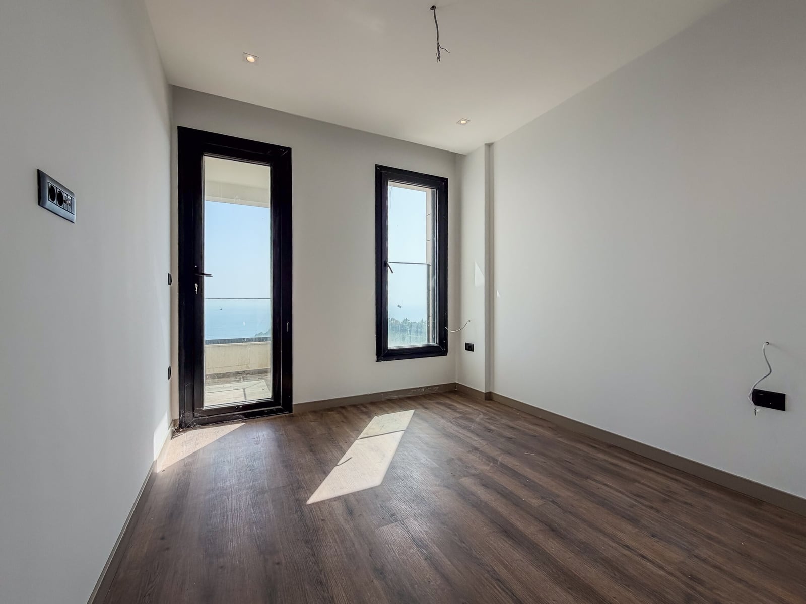 Empty room with dark laminate flooring, white walls, black door and window leading to a balcony.