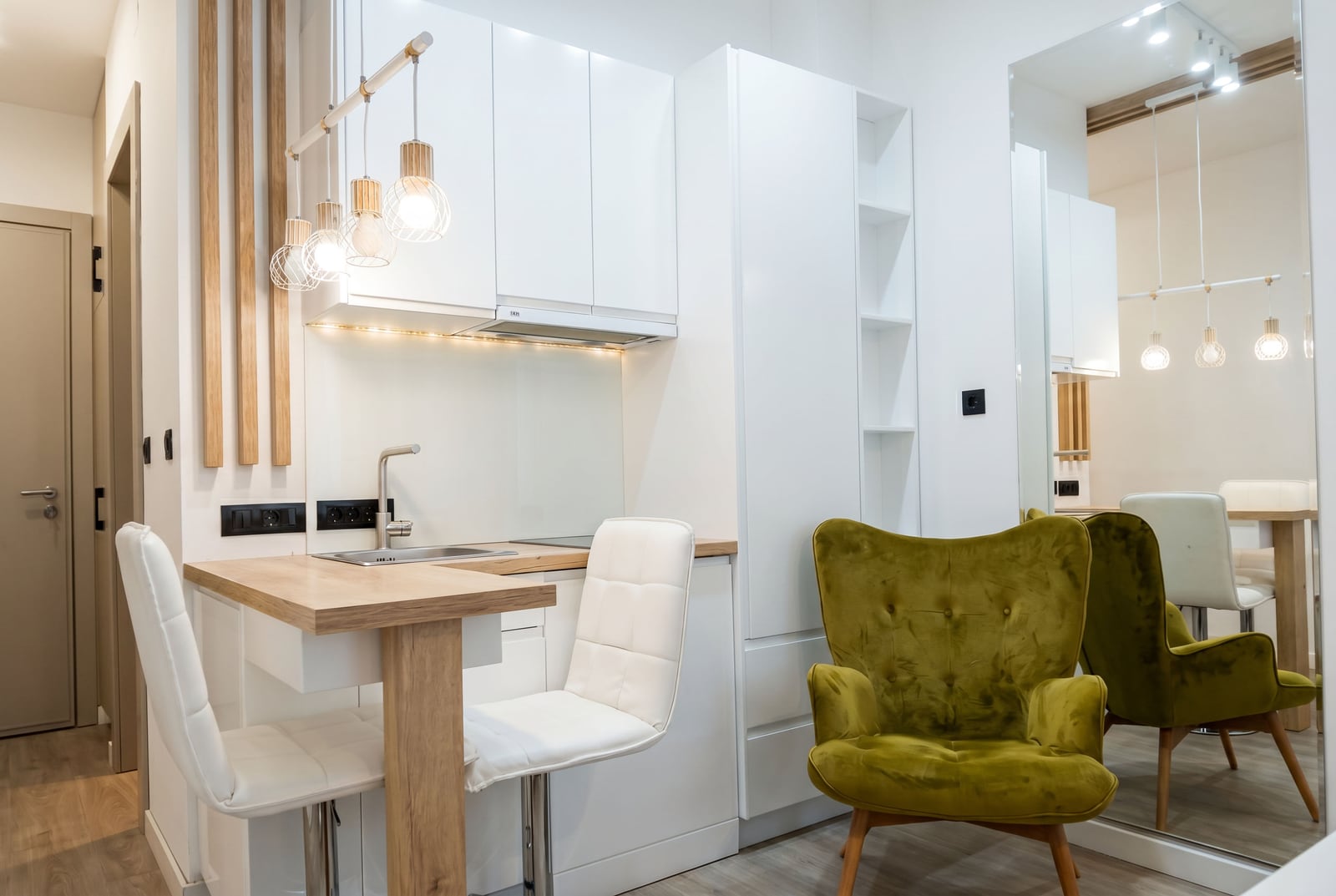 Modern kitchen in an apartment in Bečići, Montenegro: white cabinets, breakfast bar, green armchair, and stylish lighting.