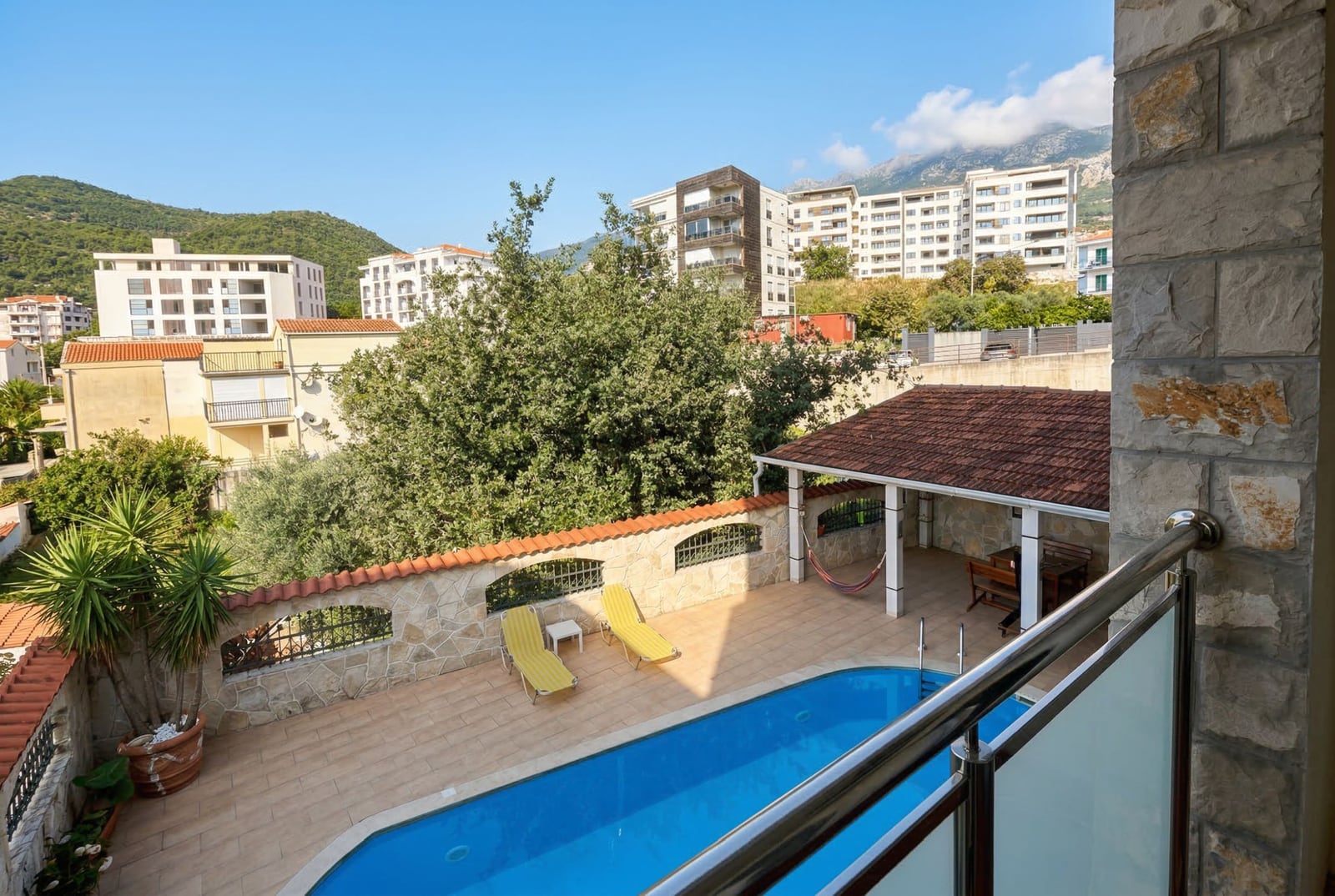 View from the balcony of the outdoor pool, sun loungers, and relaxation area at a hotel in Bečići, Montenegro.