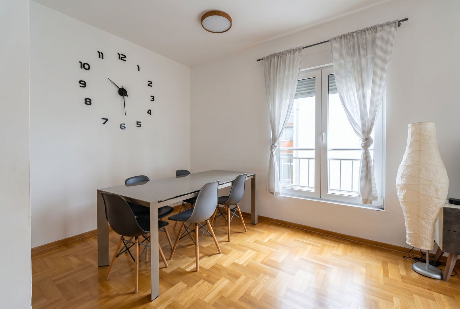 Bright living room with dining area in an apartment in Budva, Montenegro: table, Eames chairs, and wall clock.